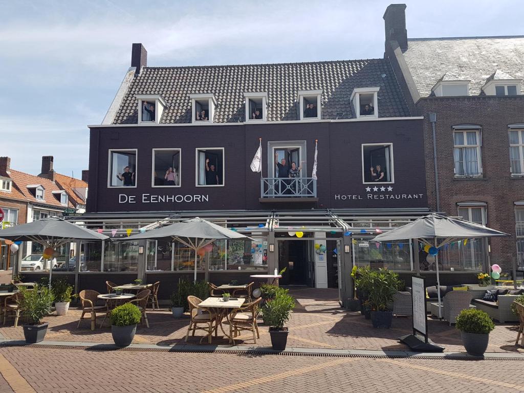 奥斯特堡De Eenhoorn的前面有桌子和遮阳伞的黑色建筑