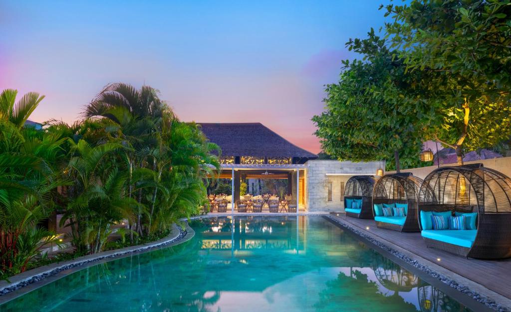 塞米亚克Avani Seminyak Bali Resort的一座房子旁的游泳池,配有蓝色的椅子
