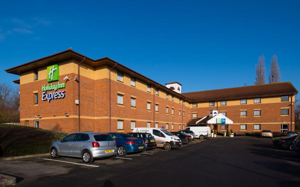 汤顿Holiday Inn Express Taunton East, an IHG Hotel的停车场内停放汽车的大型建筑