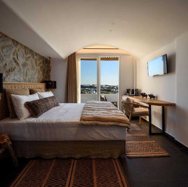米克诺斯城Vrachos Suites Mykonos的配有一张床、一张书桌和一扇窗户的酒店客房