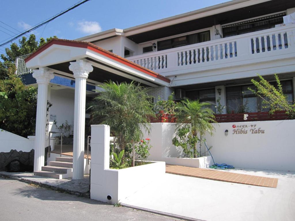 名户ホテル ハイビスヤブ的白色的房子,设有门廊和棕榈树