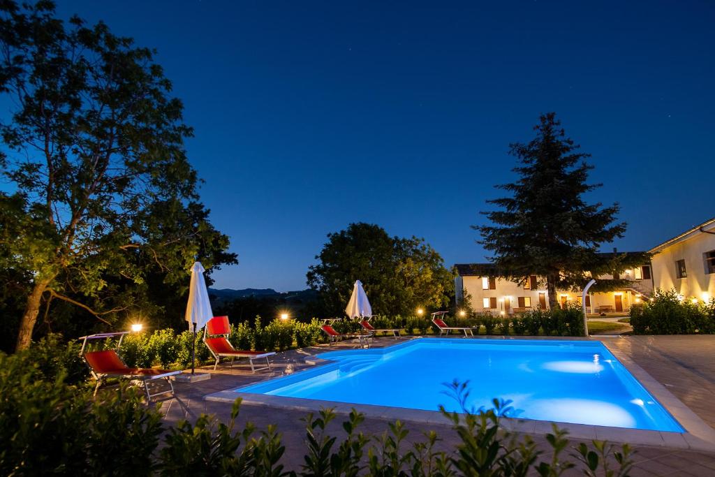 SassoferratoAgriturismo Podere Coldifico的夜间游泳池,配有椅子和遮阳伞
