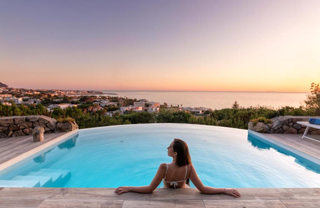 伊斯基亚Villa dei Lecci - 7 Luxury villas with private pool or jacuzzi的坐在游泳池边俯瞰大海的女人