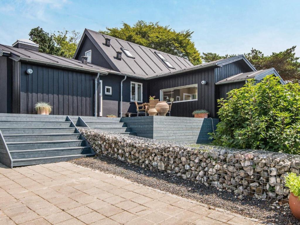 桑德比耶特6 person holiday home in Bjert的黑色的房子,有石头挡墙和楼梯