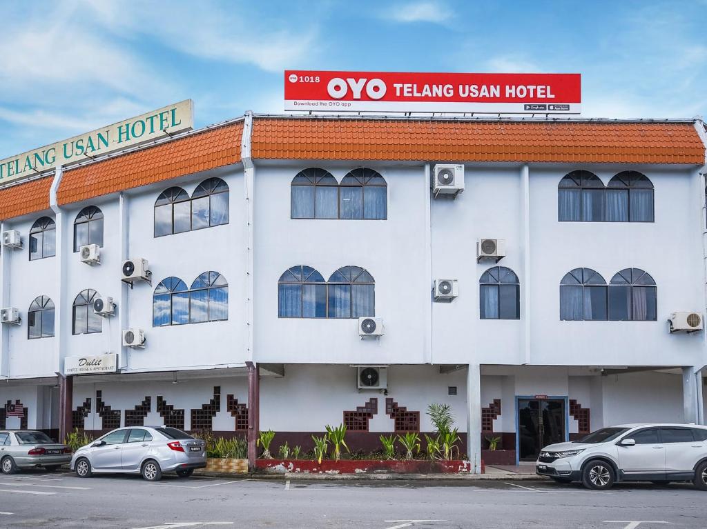 米里Super OYO 1018 Telang Usan Hotel Miri的一座白色的建筑,前面有汽车停放