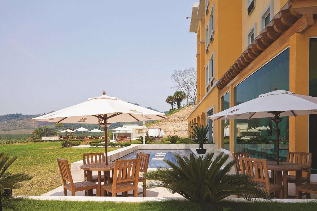 伊达尔戈州波萨里卡La Quinta by Wyndham Poza Rica的毗邻大楼的带桌子和遮阳伞的天井
