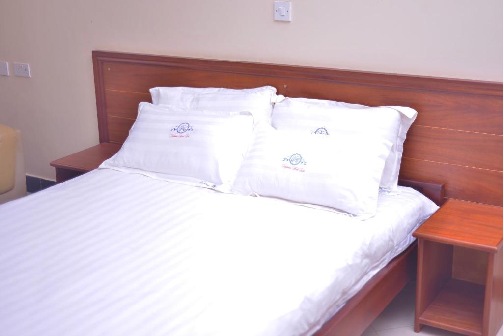 KalisizoNabisere Hotel Kalisizo的一张带白色枕头和木制床头板的床