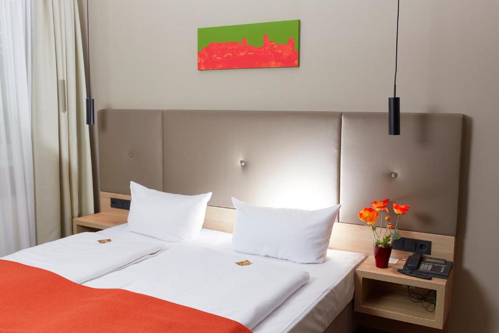 纽伦堡阿尔法酒店的酒店客房的床铺配有白色床单和橙色毯子