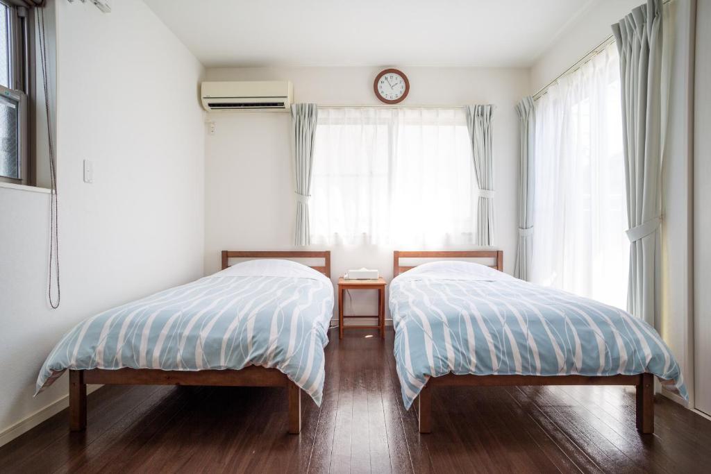 镰仓市KOSHIGOE seaside inn的卧室内的两张床,窗户上设有时钟
