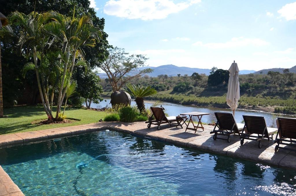 马里兰Khandizwe Kruger Villa的一个带椅子和桌子的游泳池以及一把遮阳伞