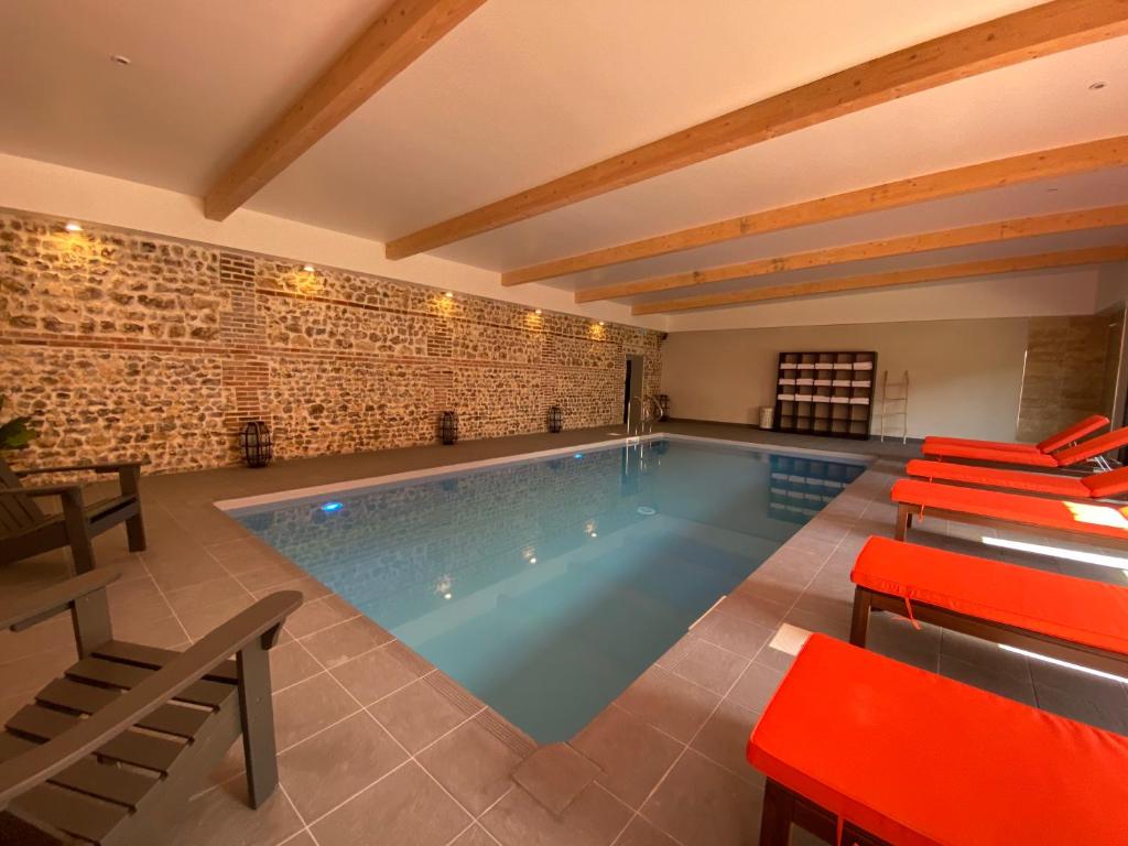 伯泽维尔Hôtel-Spa-Piscine Le Petit Castel Beuzeville-Honfleur的一个带红色桌椅的大型游泳池
