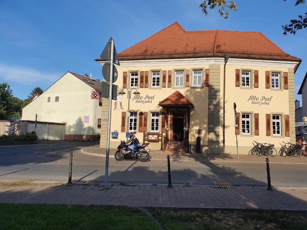 莱茵豪森Gasthof Alte Post的坐在建筑物前的摩托车上的人