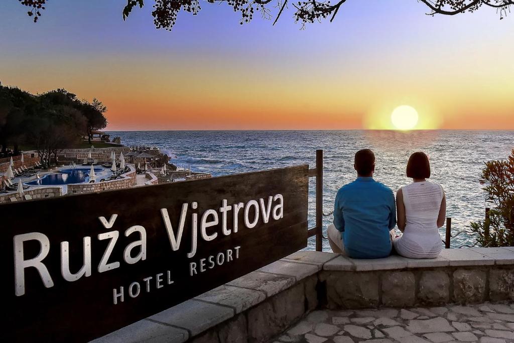多布拉沃达Ruza Vjetrova - Wind Rose Hotel Resort的两个人坐在一个看海洋的标志上