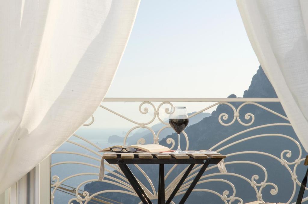 波西塔诺Casa Romelide Positano Amazing view, free parking along the street, free breakfast basket的阳台上的桌子上放着一杯葡萄酒