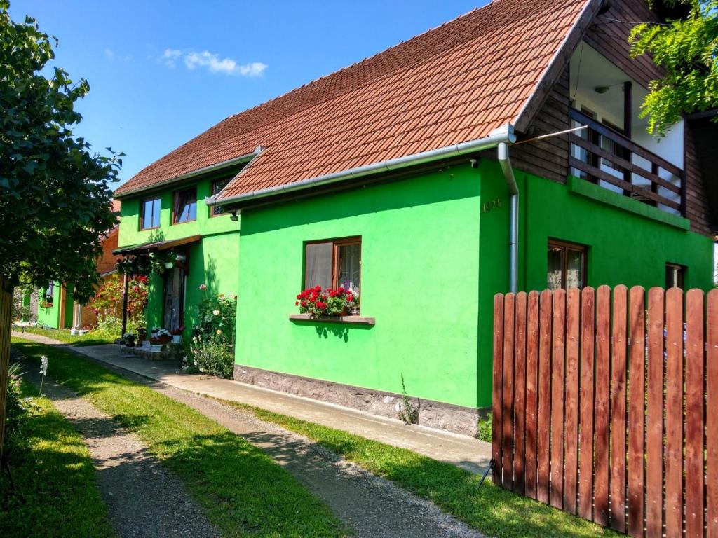 LăzareaCsergő Ildikó vendégház的一座绿色房子,设有红色屋顶和栅栏