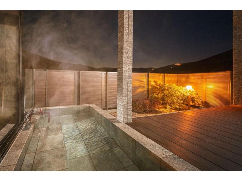 由布市YUHUROTEN YOJYOU NO BI - Vacation STAY 87032的甲板上的一个房子,晚上有热水浴缸