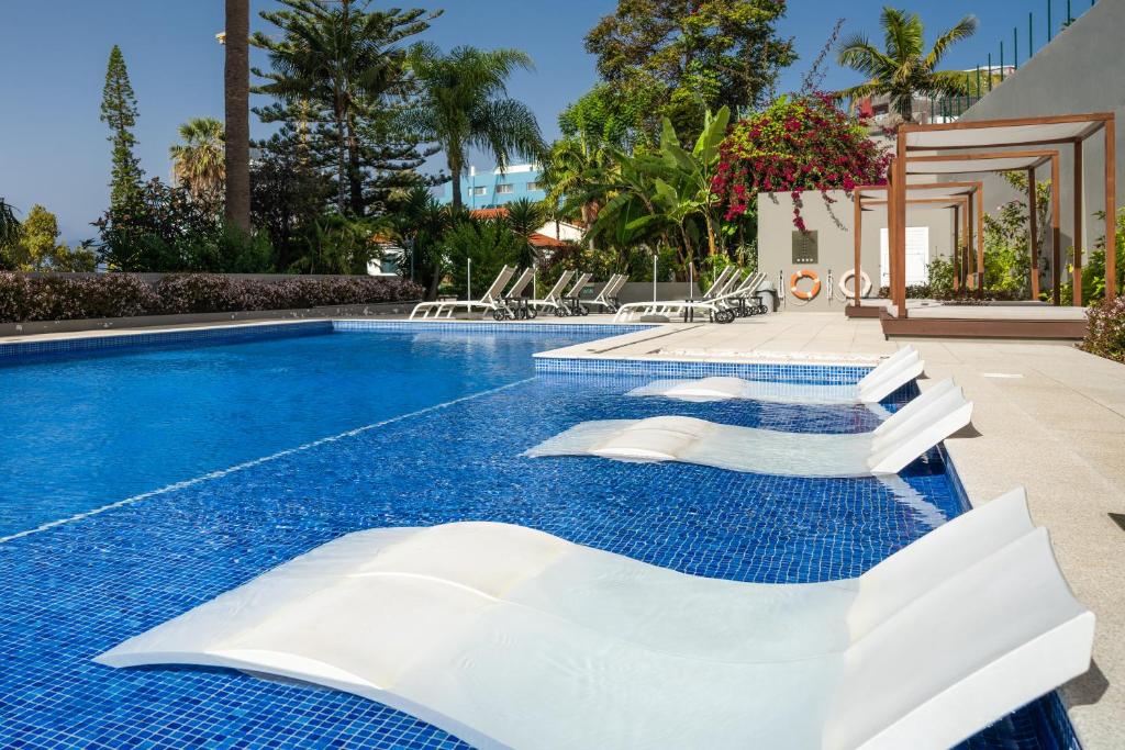 丰沙尔吉拉索尔套房酒店的度假村旁的游泳池,带白色椅子