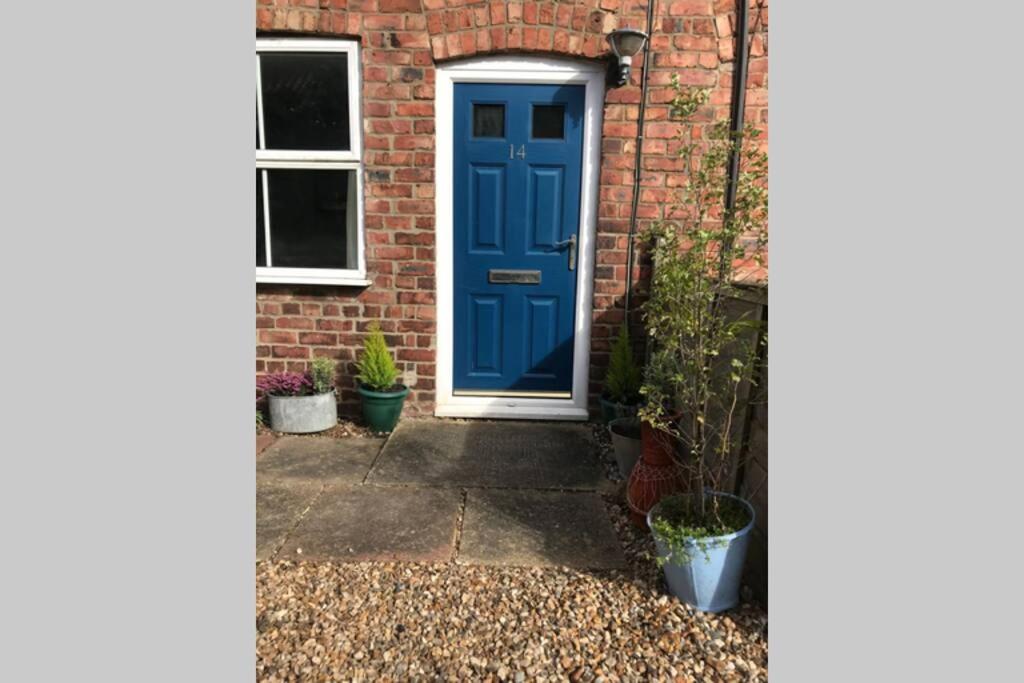 费克纳姆Attractive 2 bed cottage in Hempton Fakenham的砖房里一扇蓝色的门,里面栽有盆栽植物
