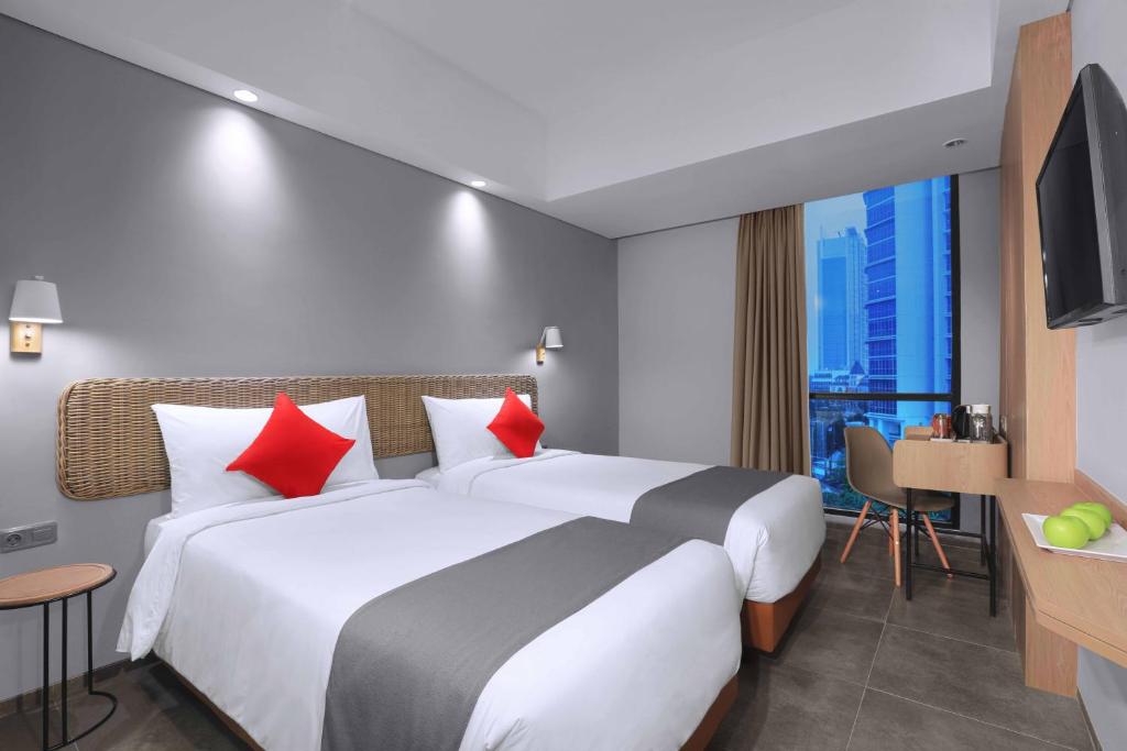 雅加达Neo Hotel Puri Indah的酒店客房配有一张带红色枕头的大床
