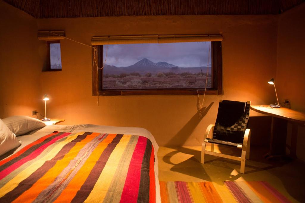圣佩德罗·德·阿塔卡马普拉内塔阿塔卡马山林小屋的卧室配有床、椅子和窗户。