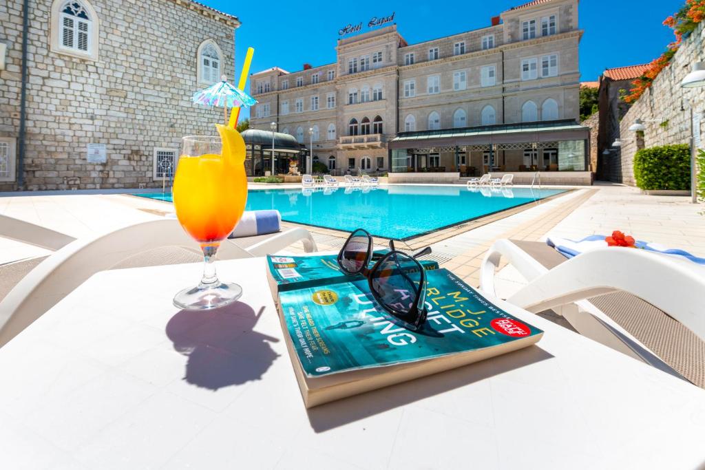 杜布罗夫尼克莱帕德酒店的游泳池旁的桌子上放着饮料和书