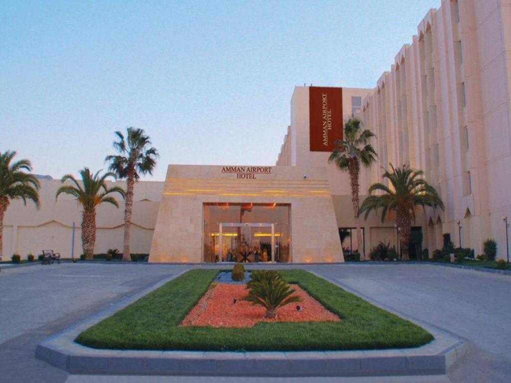 Al Qasţal安曼机场酒店的一座楼前有棕榈树的酒店