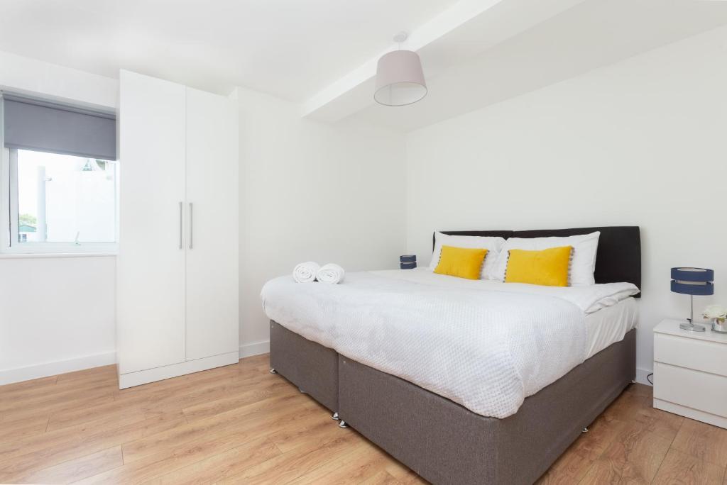 恩菲尔德Skyvillion - COZY APARTMENTS in Enfield Town With Free Parking & Wifi的白色卧室配有一张带黄色枕头的大床