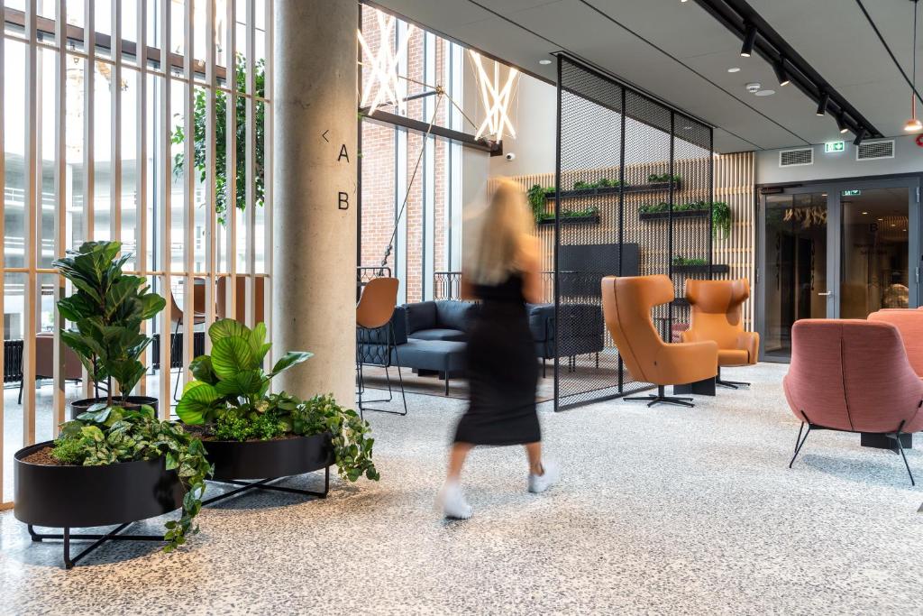 塔林Citybox Tallinn City Center的一位带着植物和椅子穿过大厅的女人