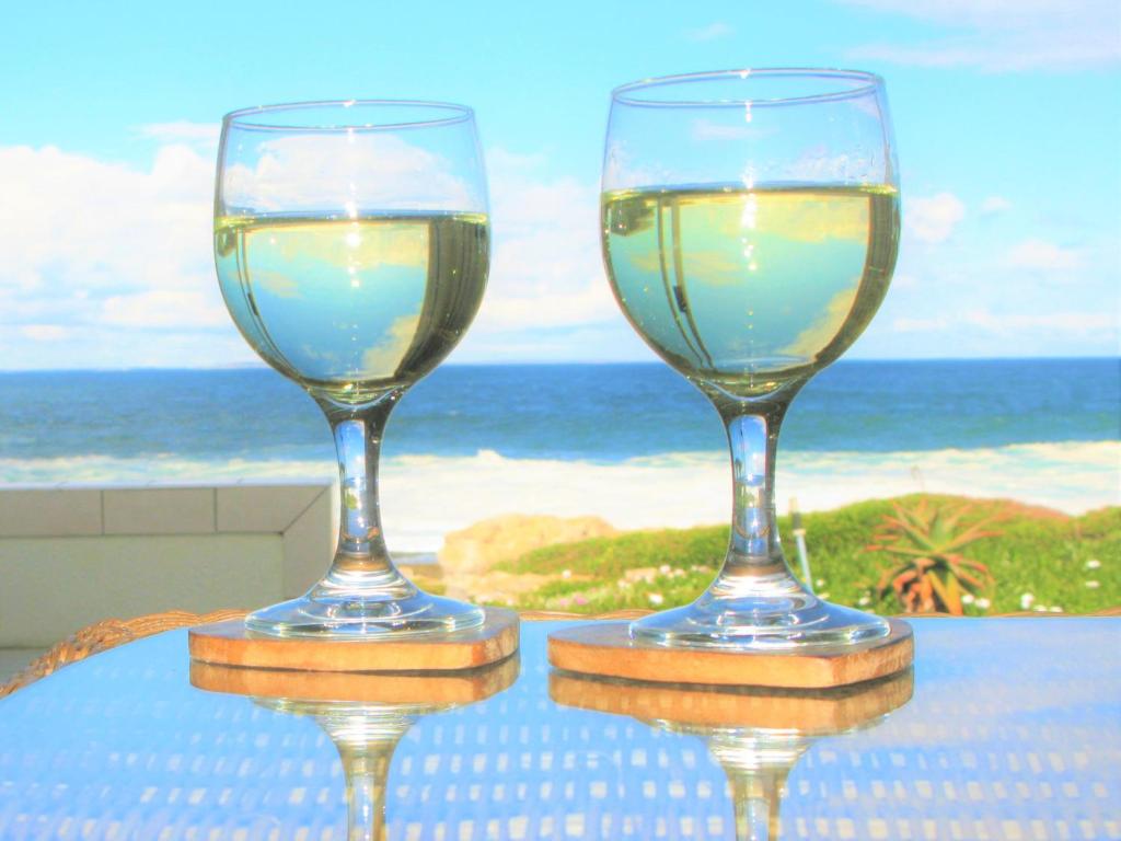 赫曼努斯Beachfront House - Hermanus Whale View的两杯酒坐在靠近大海的桌子上