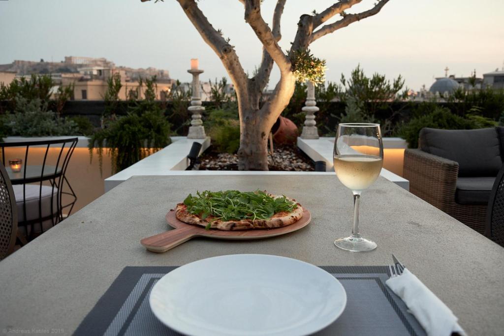 雅典雅典大厦豪华套房酒店的一张桌子,上面放着比萨饼和一杯葡萄酒