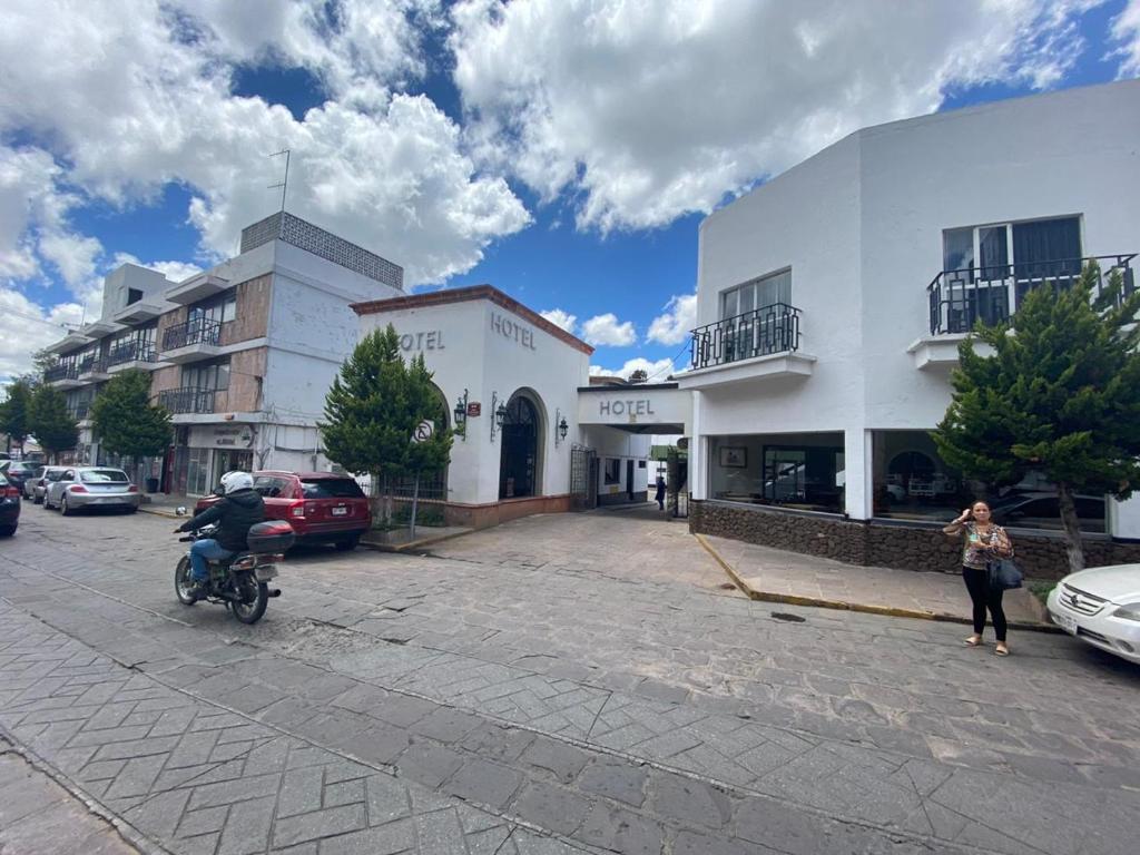 萨卡特卡斯Hotel Zacatecas Courts的骑摩托车的人在建筑物旁边的街道上