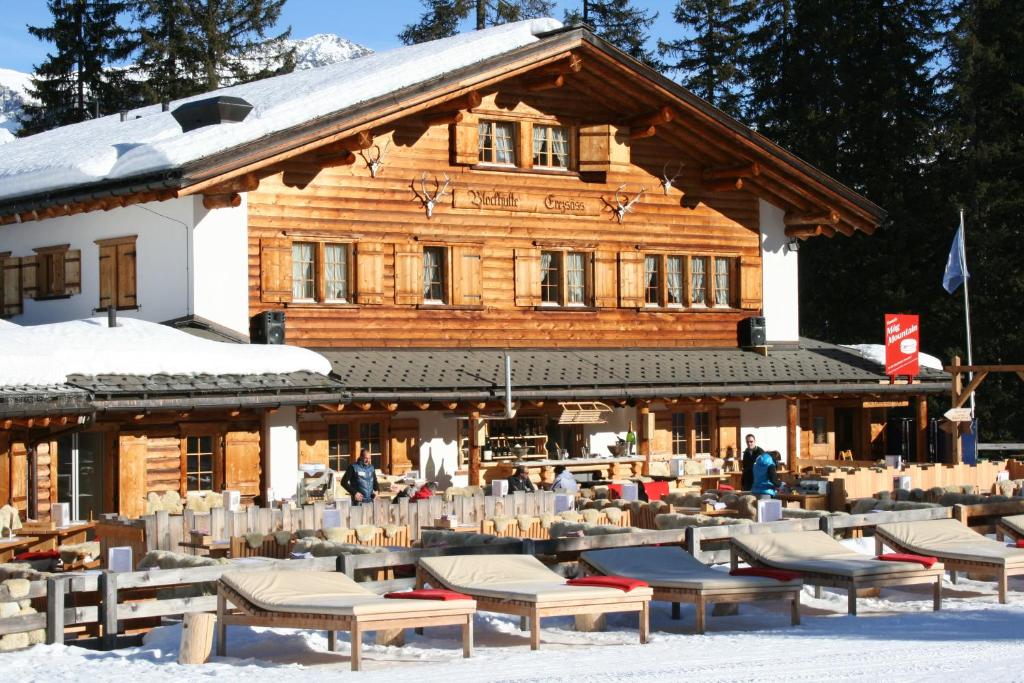 克洛斯特斯Erezsässhütte的雪地里设有桌椅的原木建筑