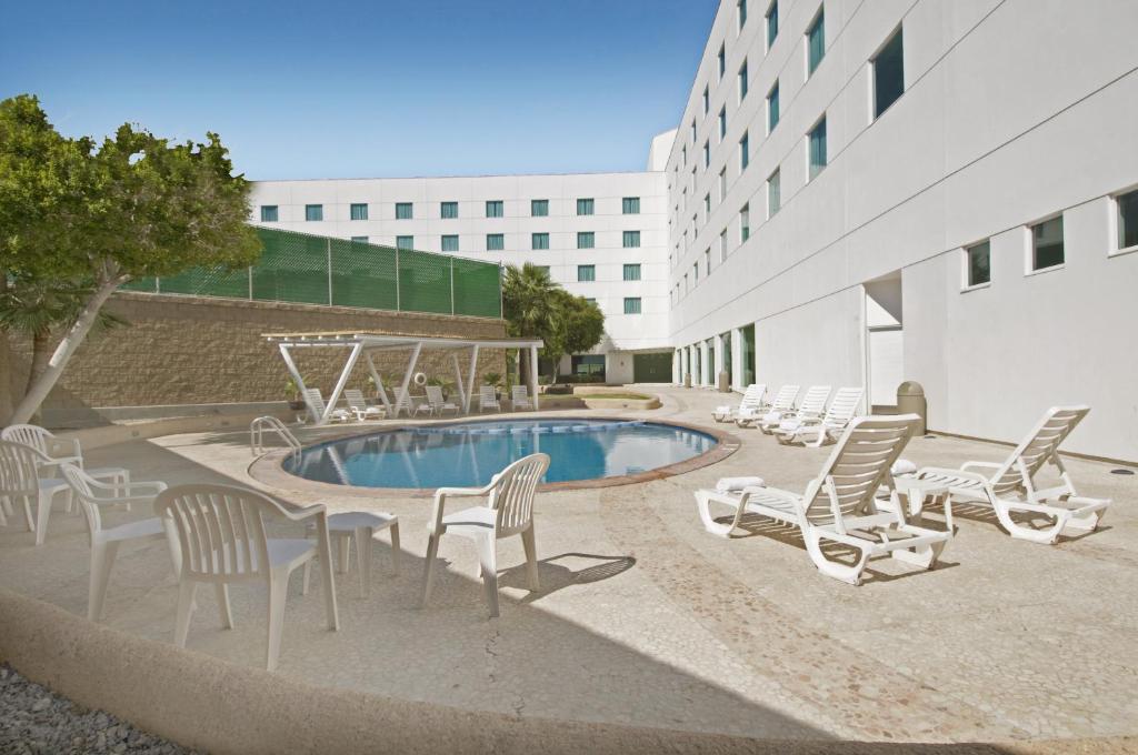 墨西卡利墨西卡利嘉年华酒店的一个带椅子的庭院、一个游泳池和一座建筑