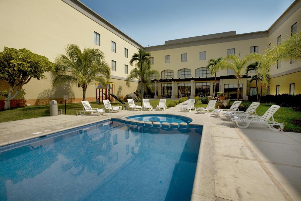 科利马科利马嘉年华酒店的一座带游泳池和椅子的酒店和一座建筑
