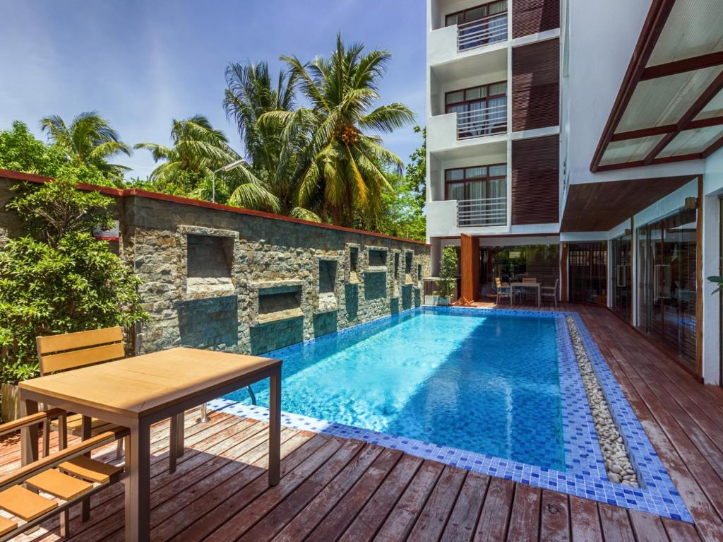 Thinadhoo马尔代夫羽毛旅馆的大楼旁的游泳池配有桌椅