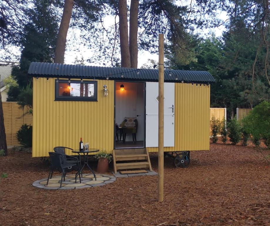 灵伍德Forest Heath Shepherd's Huts的院子里的黄色小房子,带桌子