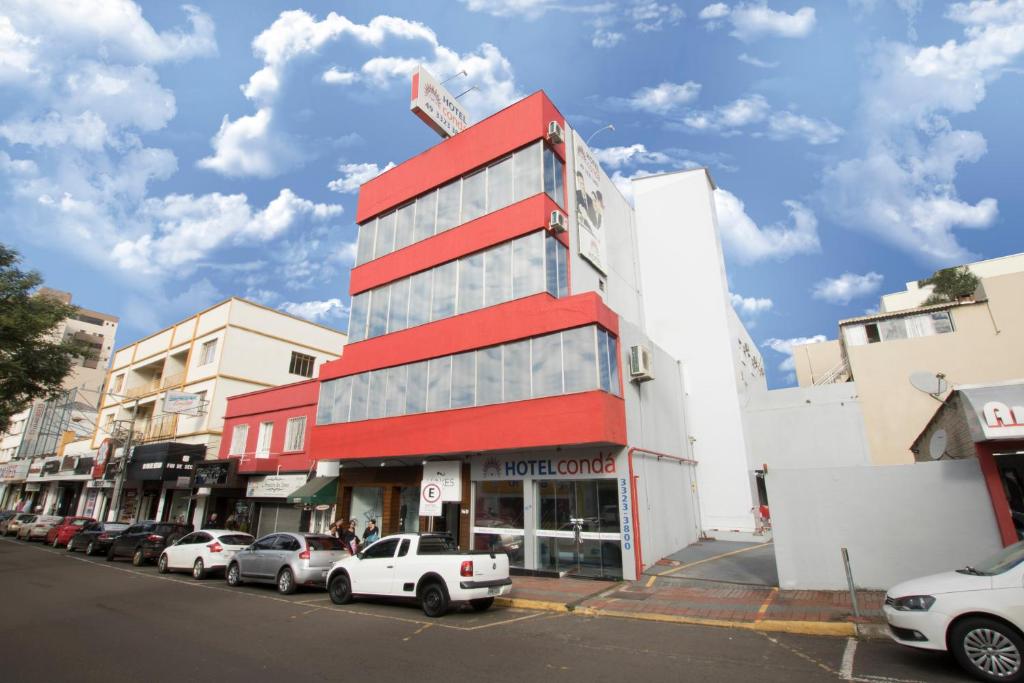 沙佩科Hotel Condá的一座红色的建筑,前面有汽车停放