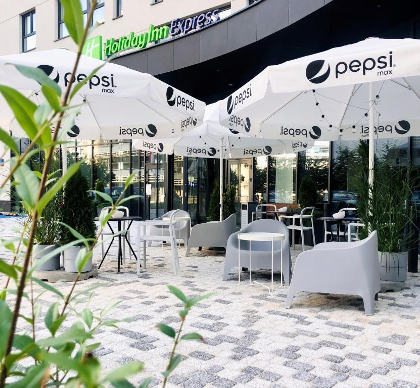 华沙Holiday Inn Express Warsaw - Mokotow, an IHG Hotel的庭院配有白色的桌椅和遮阳伞。
