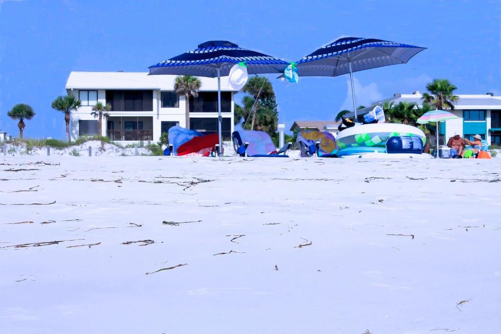 布雷登顿海滩Anna Maria Island Beach Sands 101的海滩上有两个蓝色的遮阳伞,还有一座建筑