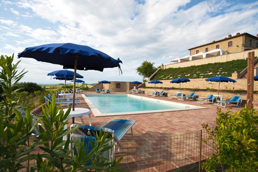渥尔特拉Agriturismo Santa Vittoria的一座带蓝色遮阳伞和椅子的游泳池位于一座建筑旁边