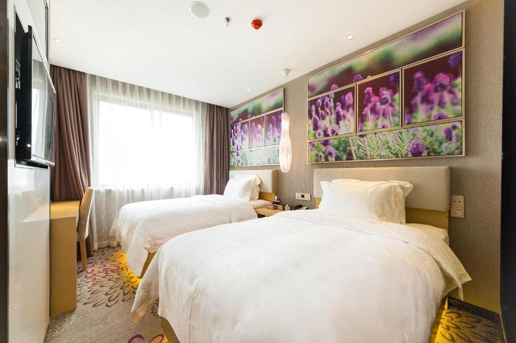 威海Lavande Hotels Weihai Weigao Square Branch的两张床铺,位于酒店客房,墙上挂着鲜花