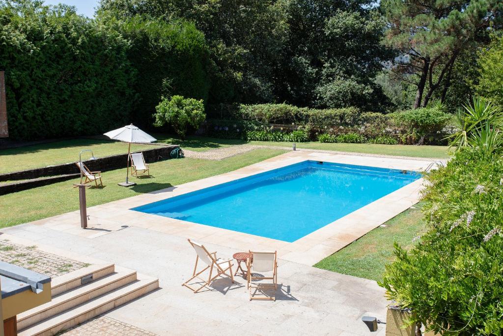 卡米尼亚Liiiving in Caminha | Countryside Pool House的一个带两把椅子和遮阳伞的游泳池