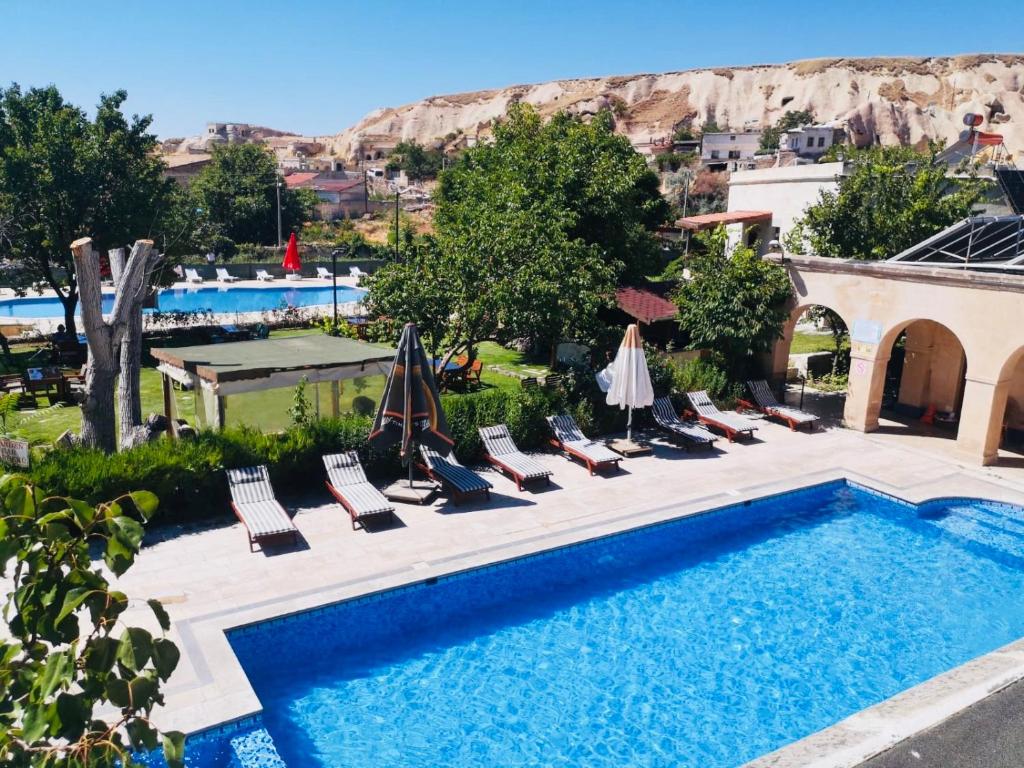 于尔居普麦里斯洞穴酒店的毗邻度假酒店的带椅子和遮阳伞的游泳池
