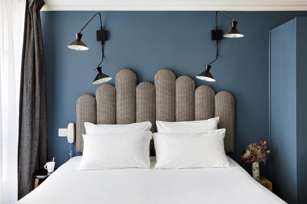 巴黎巴拉迪酒店的一间卧室拥有蓝色的墙壁,配有一张带白色枕头的床。