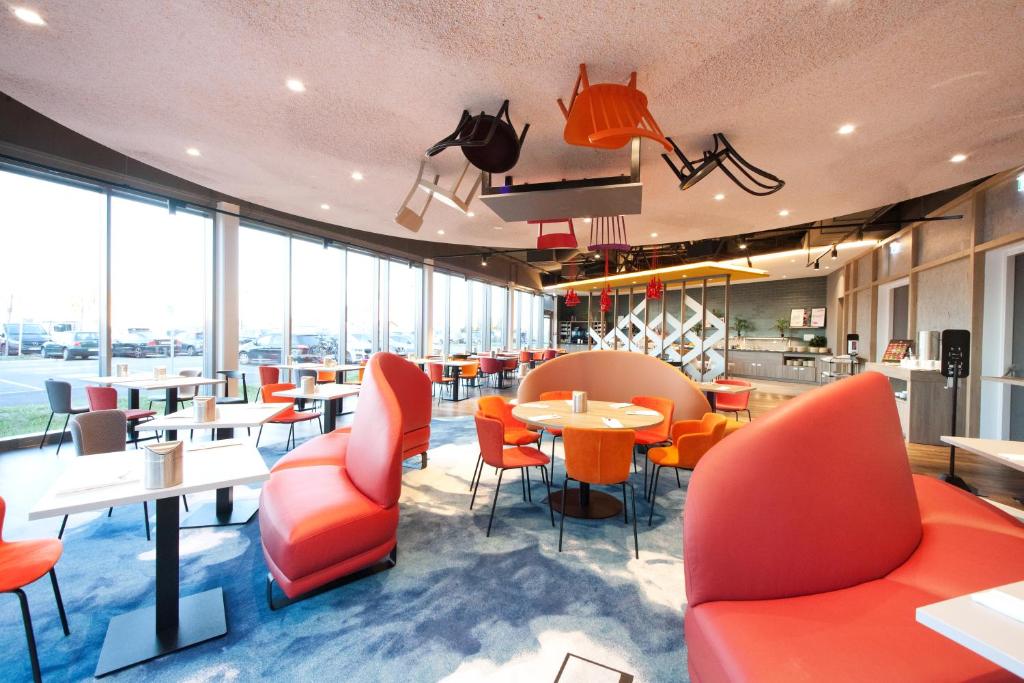 帕恩多夫ibis Styles Parndorf Neusiedler See的餐厅设有橙色椅子和桌子以及窗户。