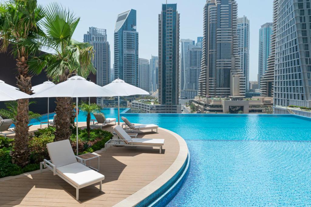 迪拜Jumeirah Living Marina Gate Hotel and Apartments的一个带椅子和遮阳伞的游泳池,并享有城市天际线