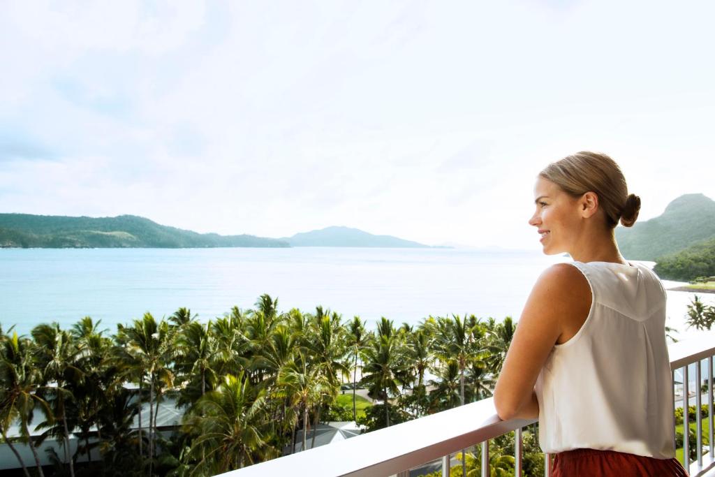 汉密尔顿岛珊瑚景酒店的站在一个眺望着水面的阳台上的女人