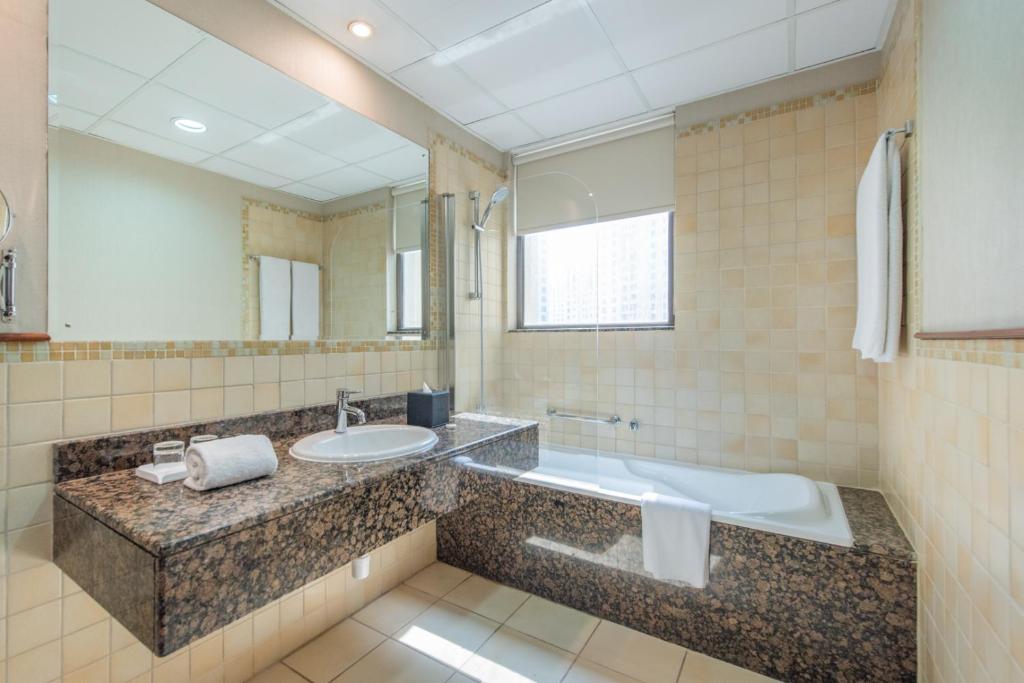 迪拜Suha JBR Hotel Apartments的一间带水槽、浴缸和镜子的浴室