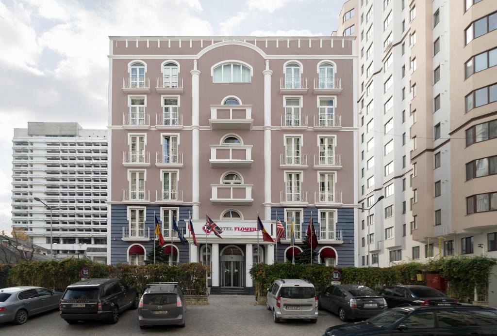 基希讷乌Flowers Hotel的一座粉红色的建筑,汽车停在停车场
