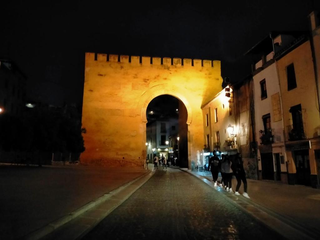 格拉纳达MAJESTUOSA ALHAMBRA Nuevo apartamento的城堡的拱门,晚上有人沿着街道走